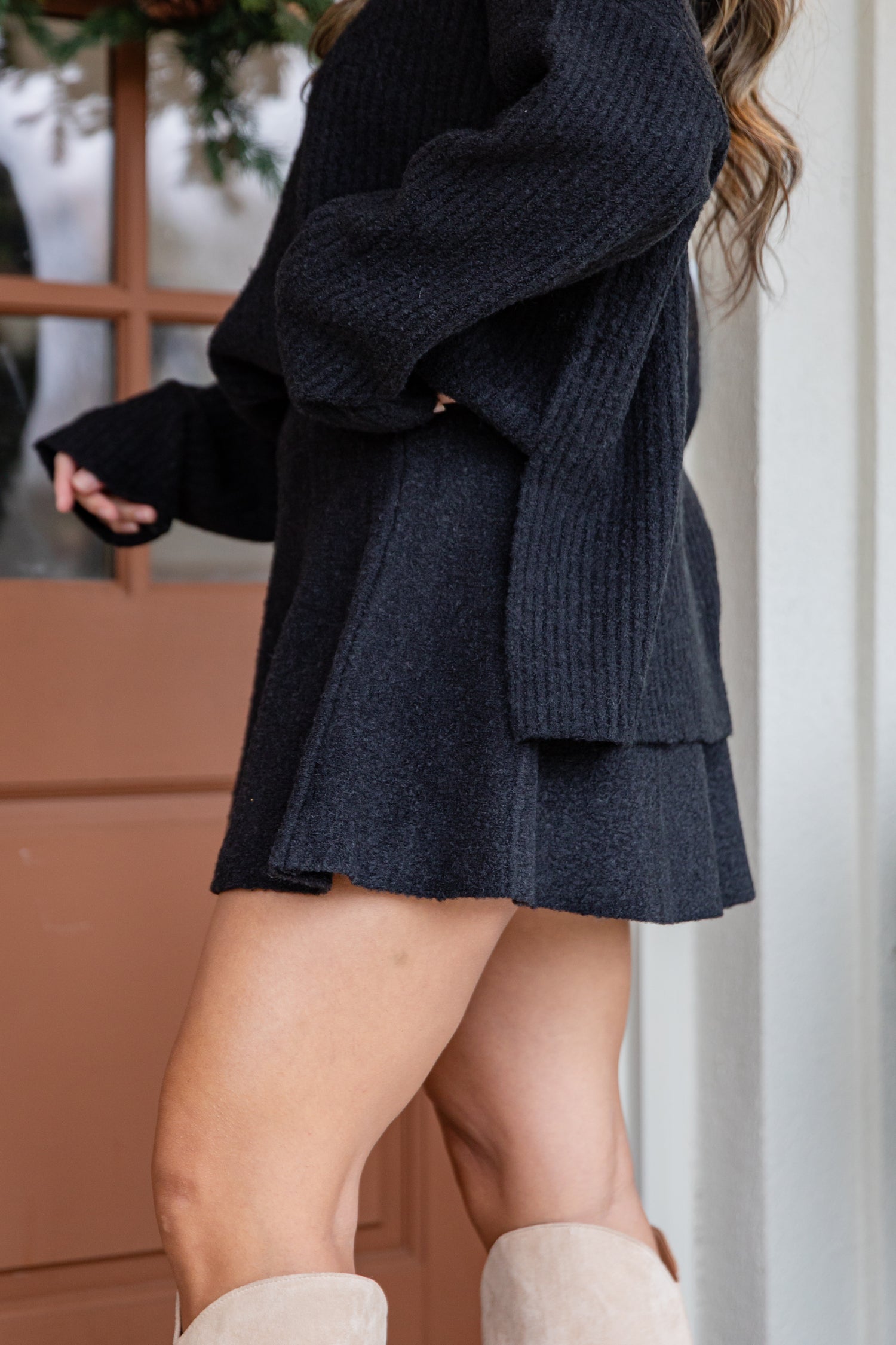 Person wearing a dark blue sweater and skirt with beige boots indoors.