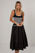A woman modeling a sleeveless midi dress with a black and white horizontally striped bodice and a full black tiered skirt, paired with tan pointed-toe heels against a plain light gray studio background.