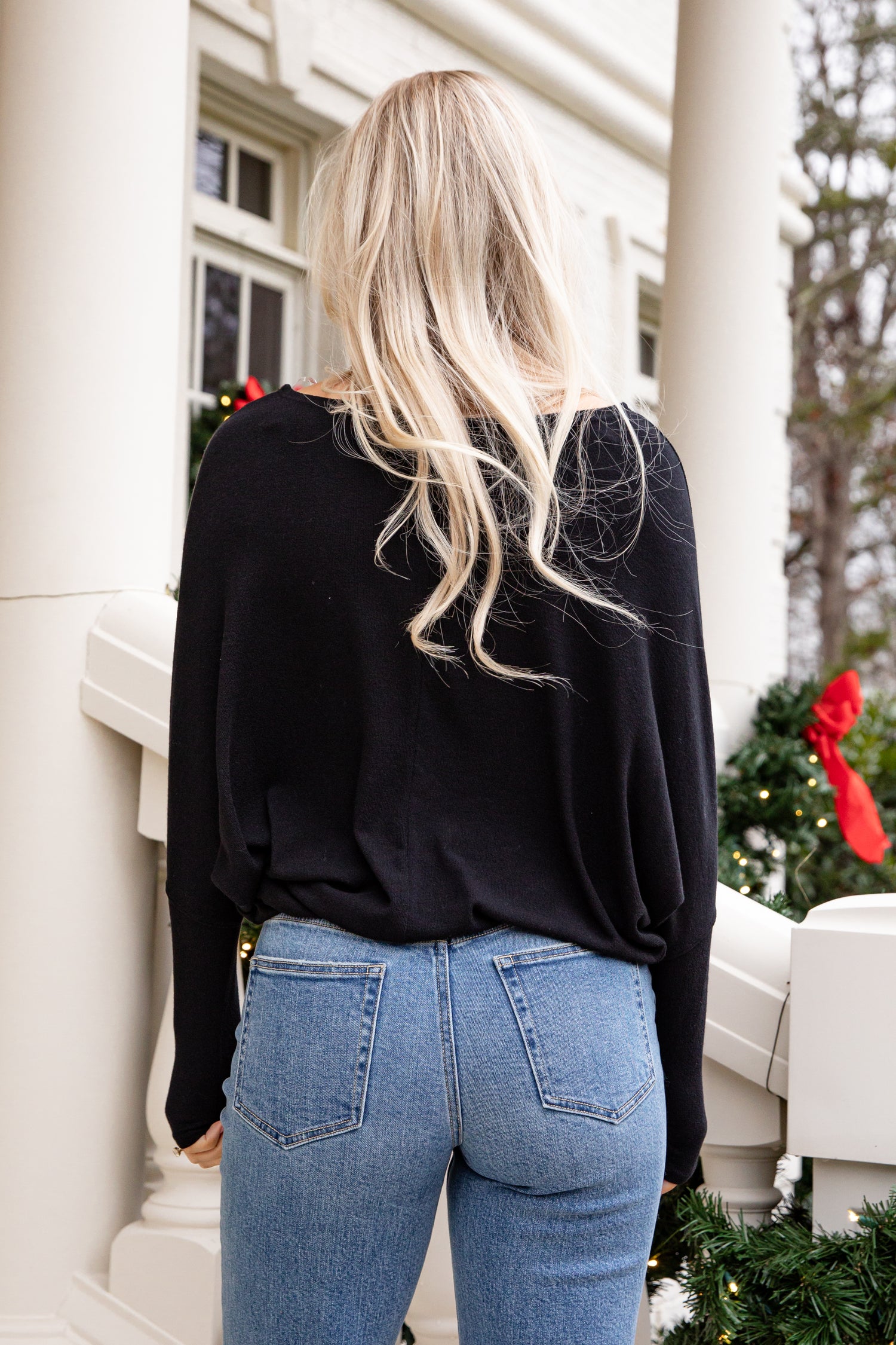 Person wearing a black top and blue jeans standing in front of a building with decorative elements.