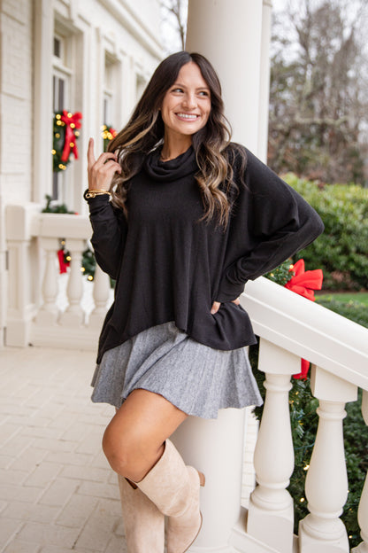 Woman in black sweater and gray skirt standing on a porch with Christmas decorations.