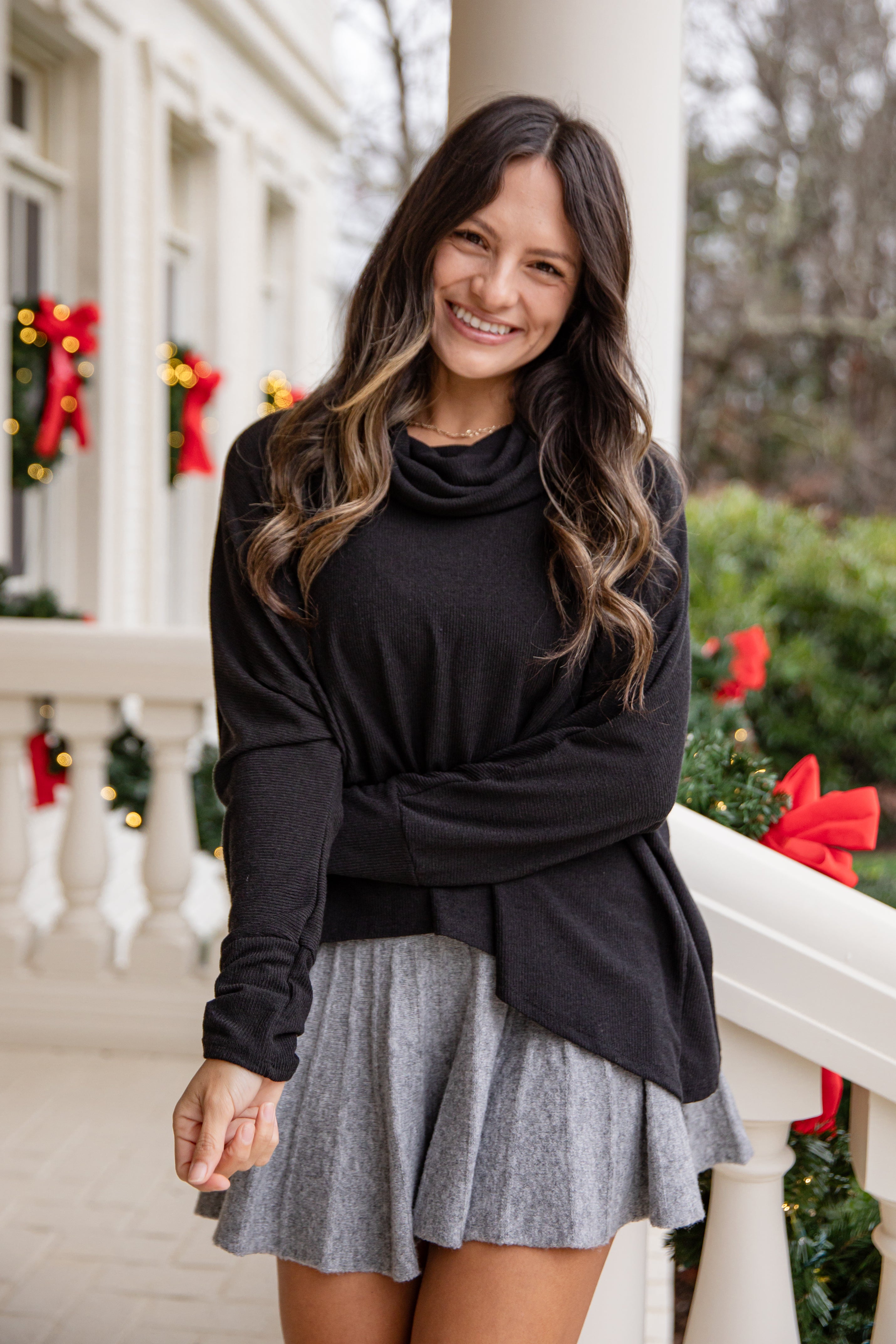 Woman wearing a black sweater and gray skirt on a decorated porch