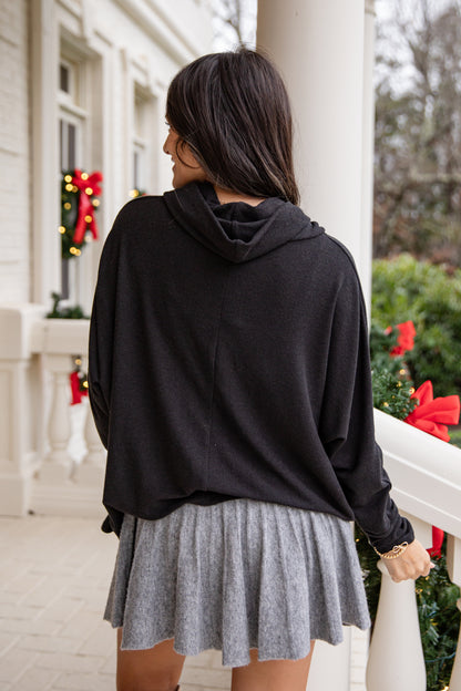 Person wearing a black hoodie and gray skirt on a porch with holiday decorations.