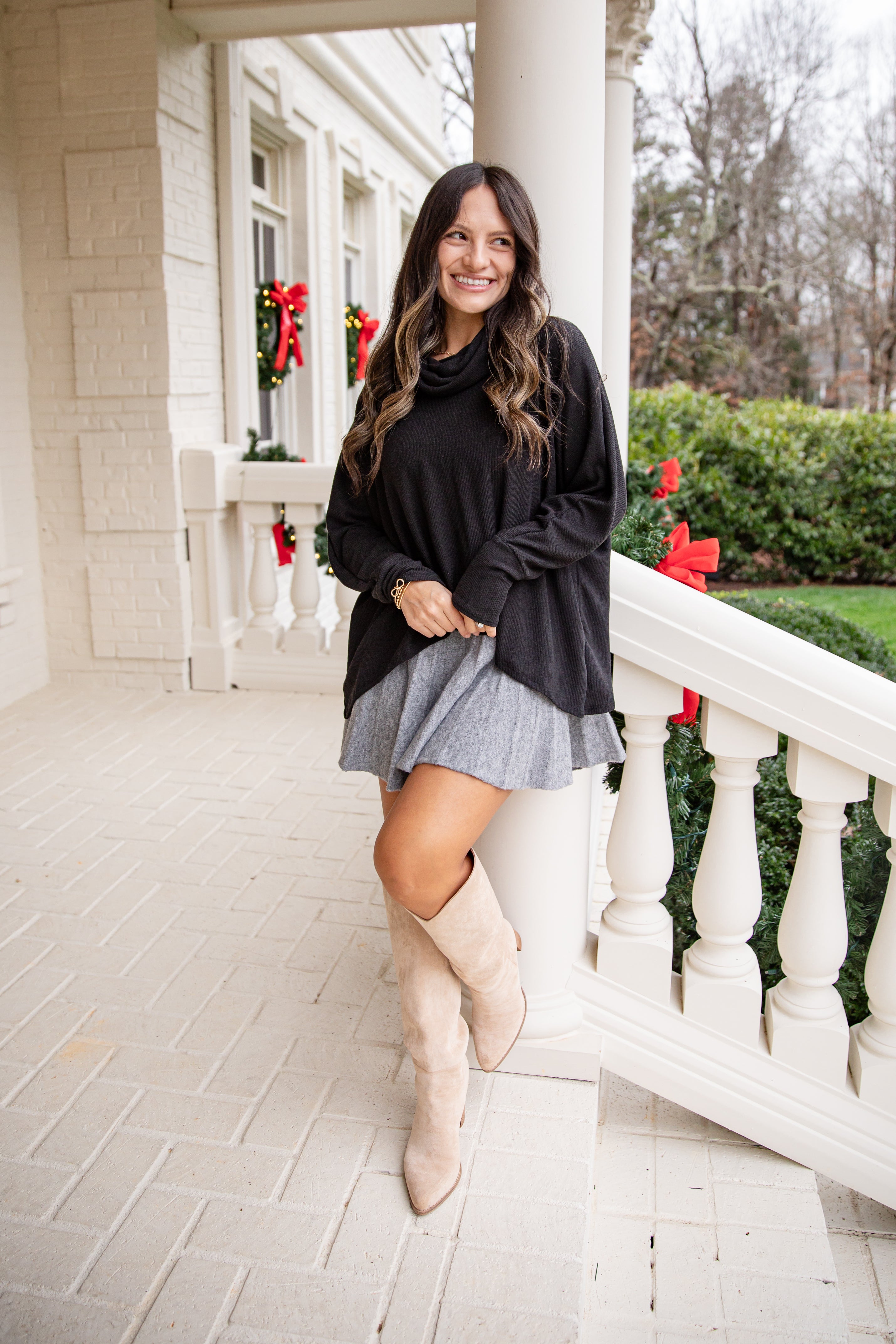 Woman in black sweater and gray skirt standing on a porch with decorative bows.