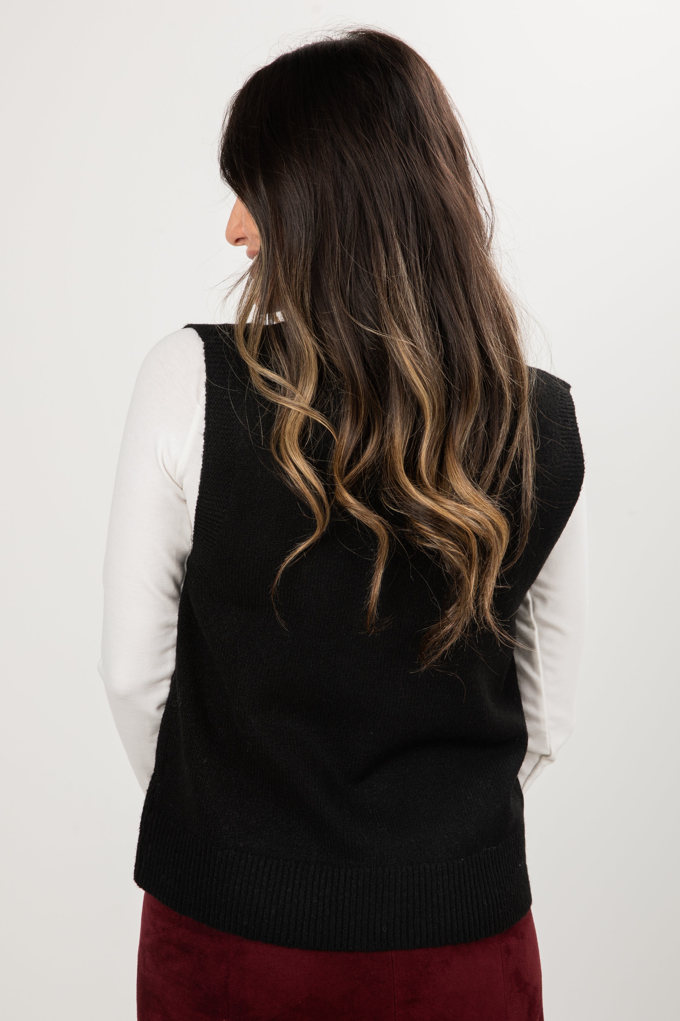 Person wearing a black sweater vest over a white long-sleeve shirt on a plain background