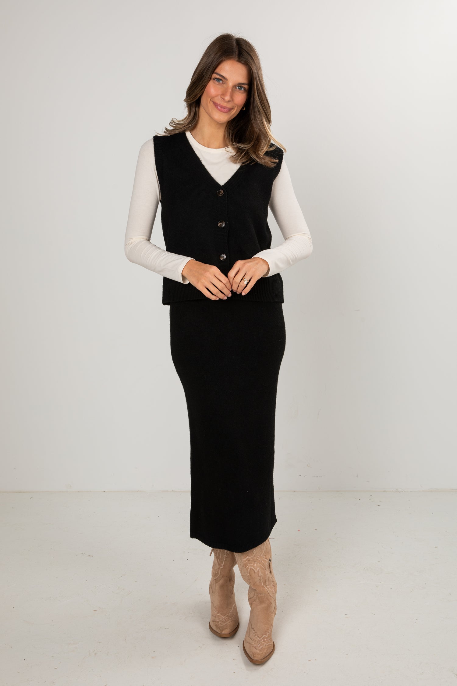 Woman wearing a black dress with a white shirt and beige boots on a white background