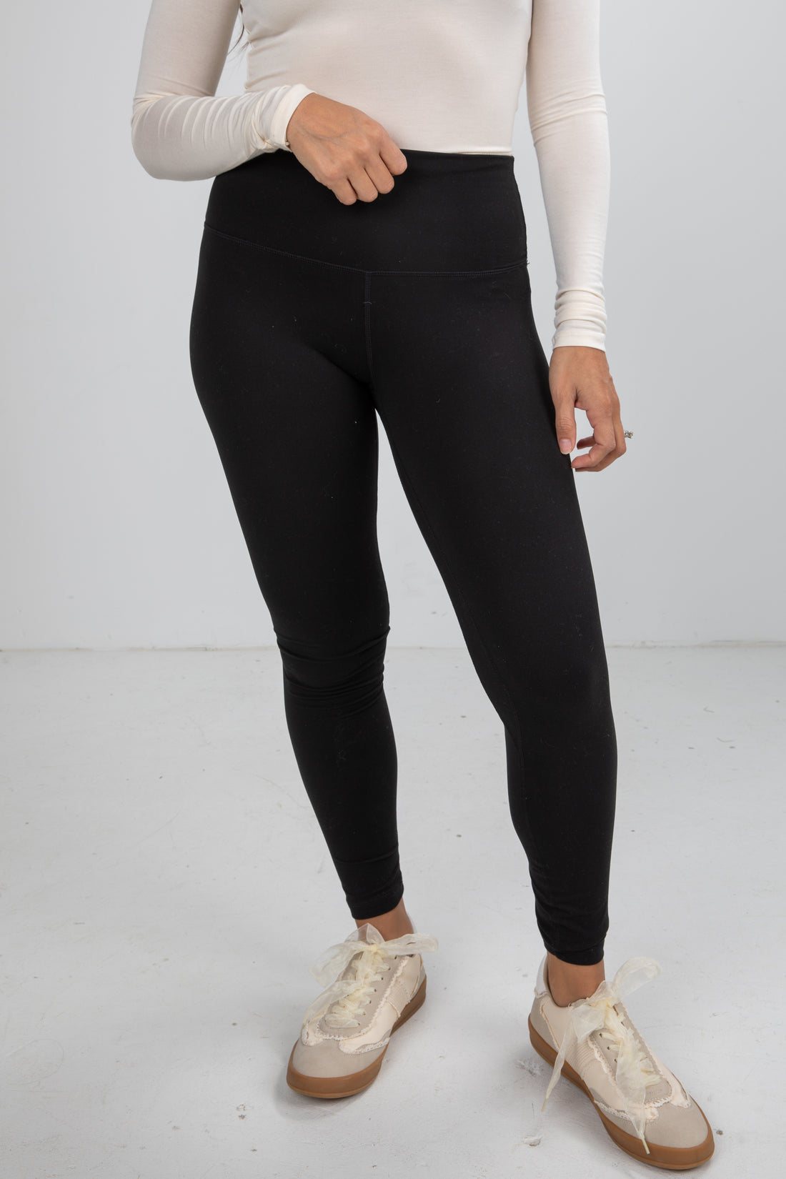 Person wearing black leggings and white sneakers on a plain background