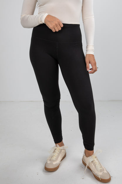 Person wearing black leggings and white sneakers on a plain background