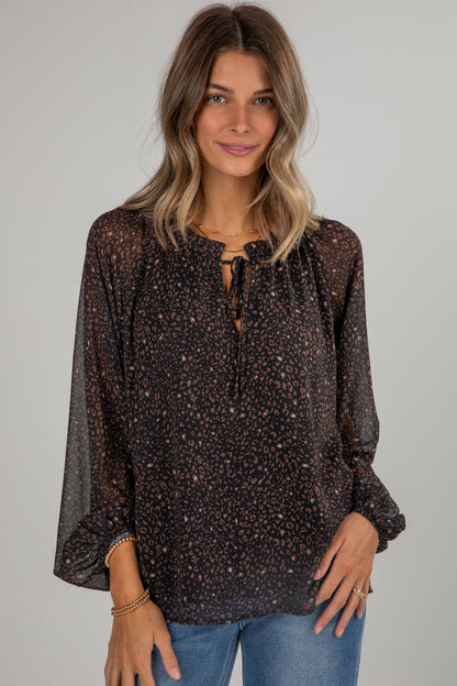 Woman wearing a dark patterned blouse with sheer sleeves against a plain background