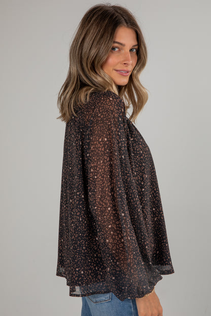 Woman wearing a sheer brown blouse with a subtle pattern on a plain background