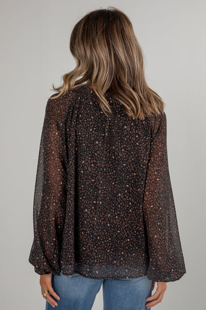 Person wearing a patterned blouse with long sleeves on a plain background