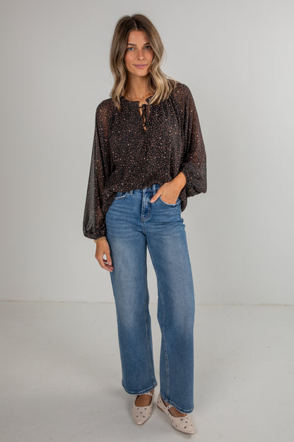 Woman wearing a patterned top and blue jeans against a plain background