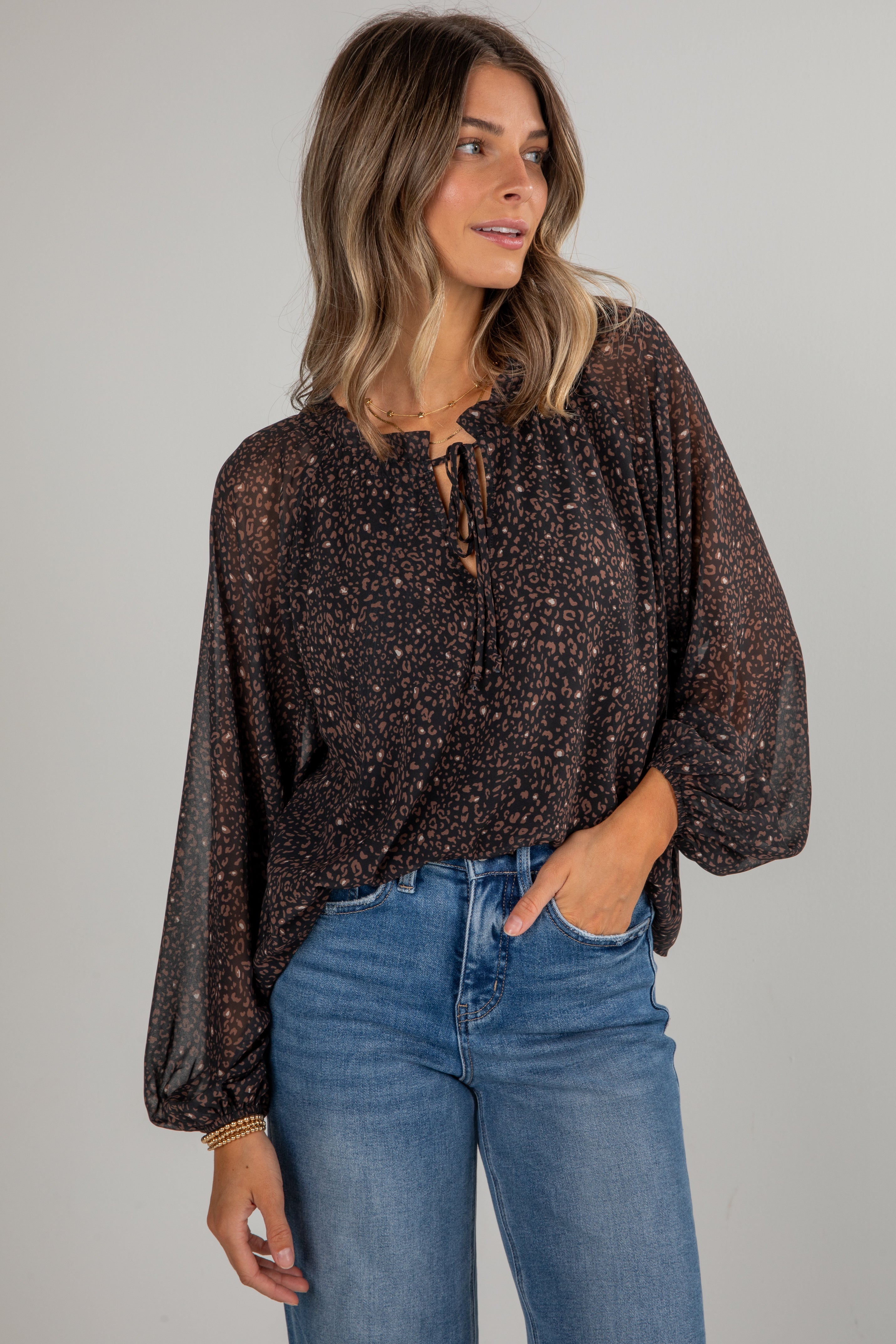 Woman wearing a brown patterned blouse and blue jeans against a gray background