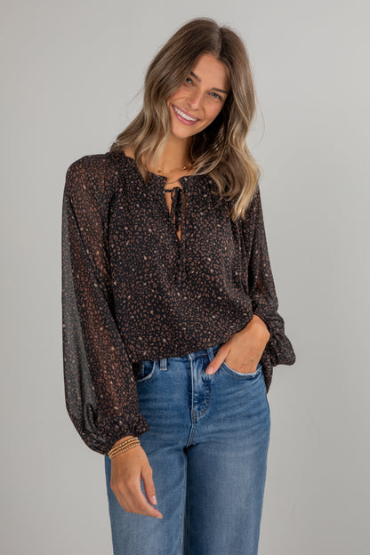 Woman wearing a patterned blouse and blue jeans against a gray background