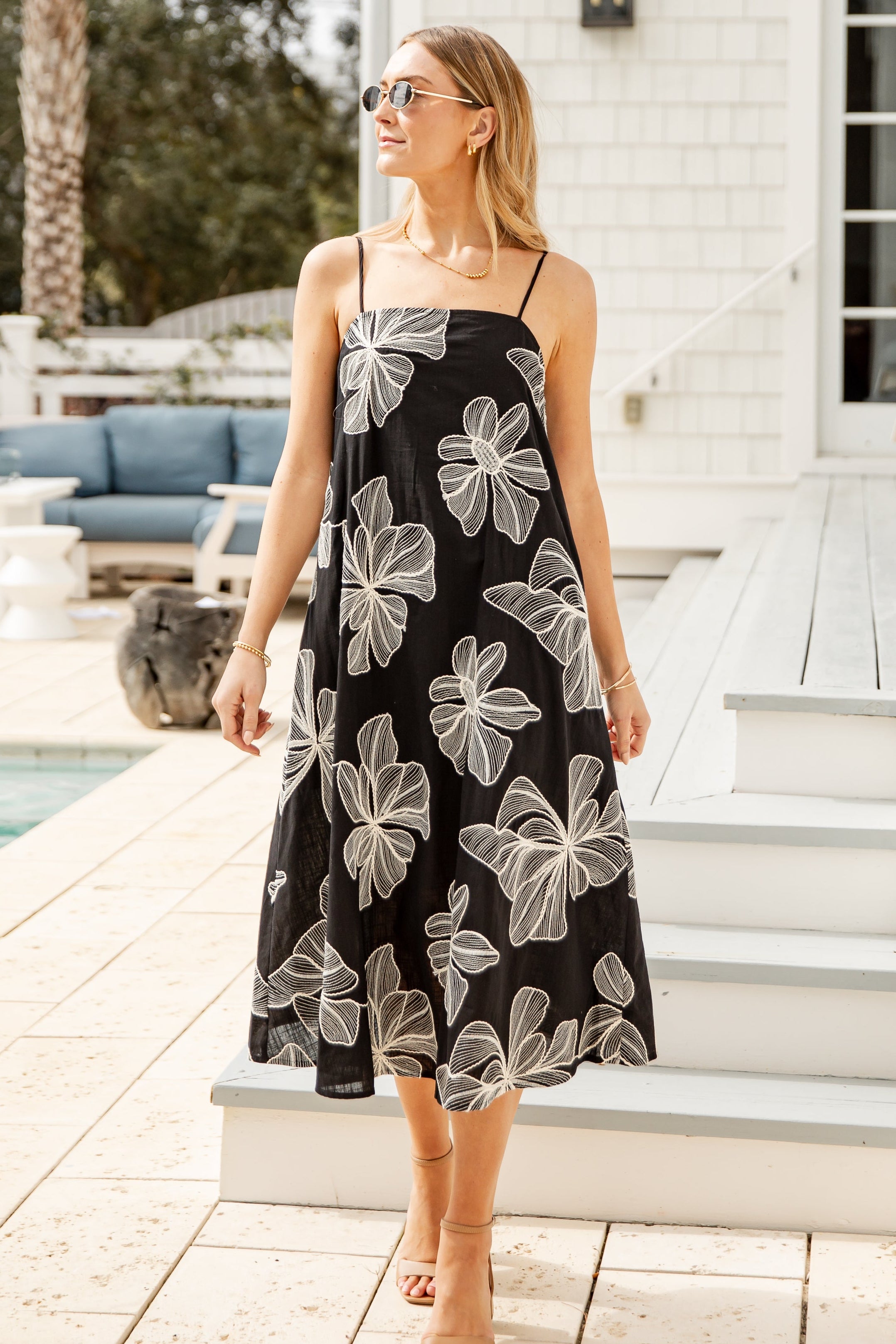 Woman in a black floral dress standing on a wooden deck by a poolside.
