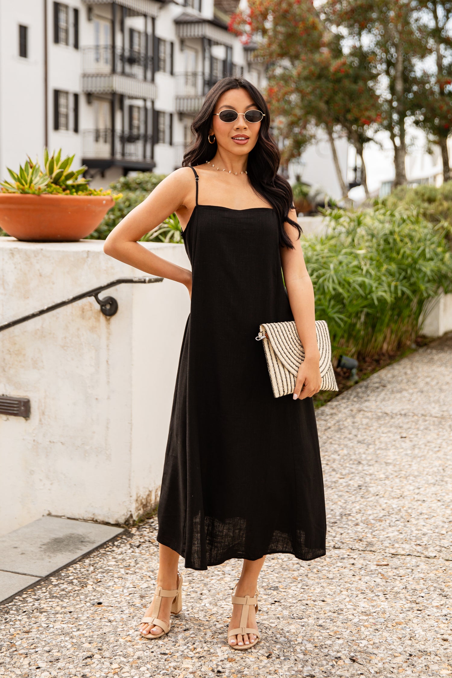 Woman in a black dress standing outdoors with a building and plants in the background