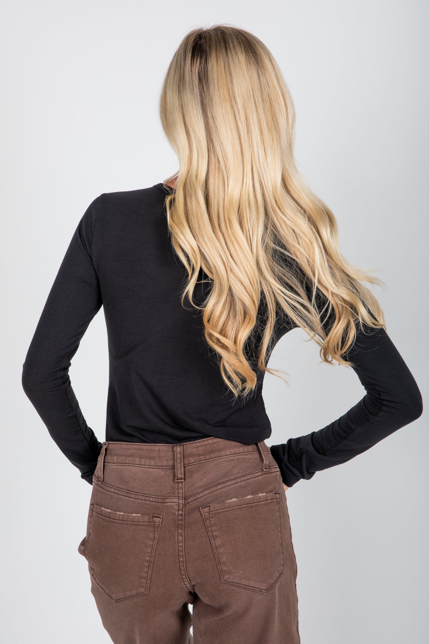 Person wearing a black long-sleeve top and brown pants with a plain background