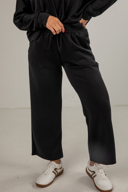 Person wearing black pants and white sneakers on a plain background