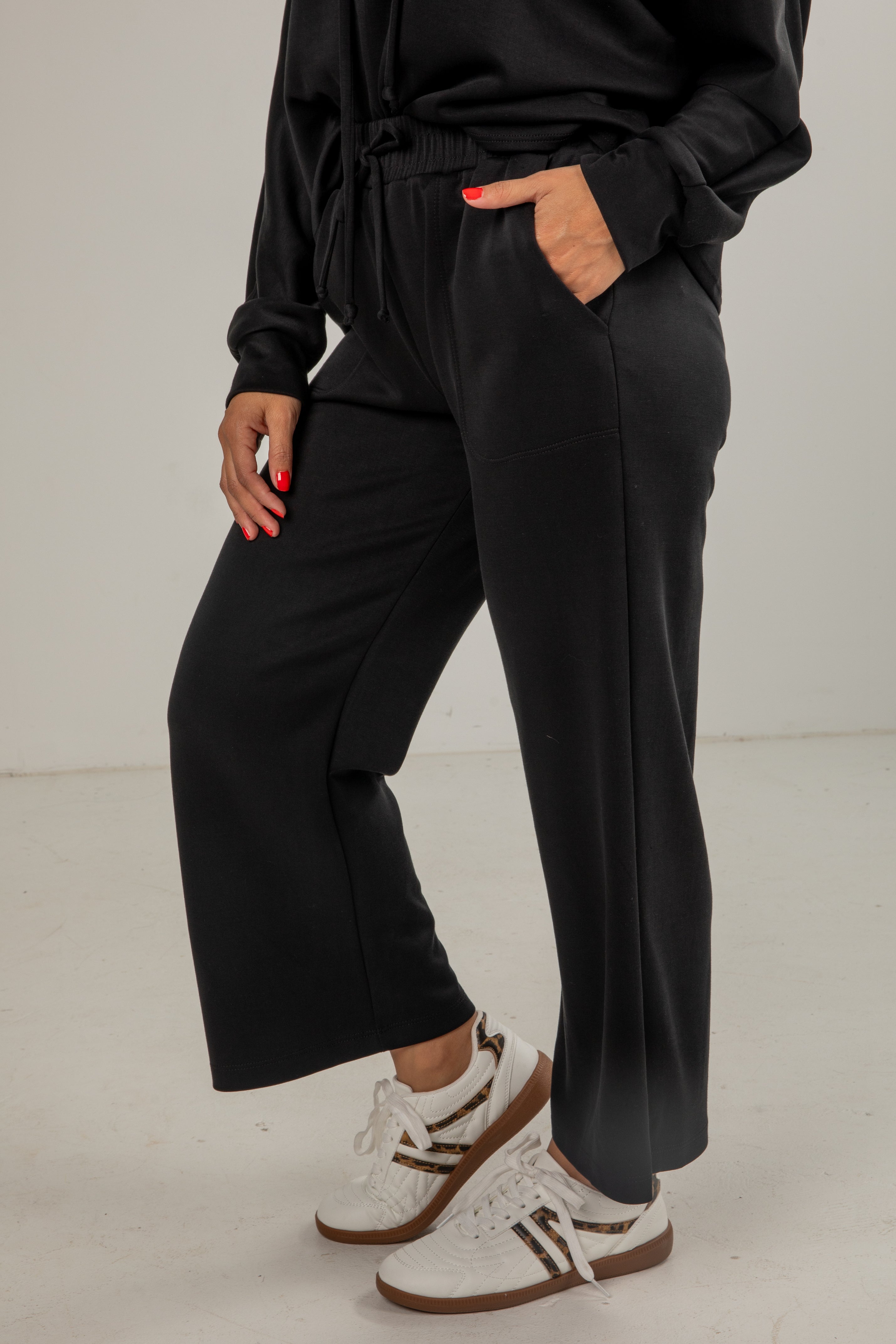 Person wearing black pants and white sneakers on a plain background