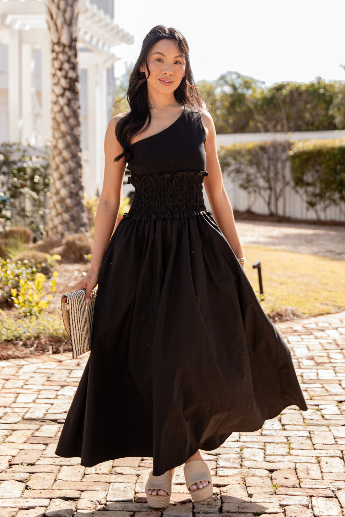 Woman in a black dress standing on a stone path with a garden background