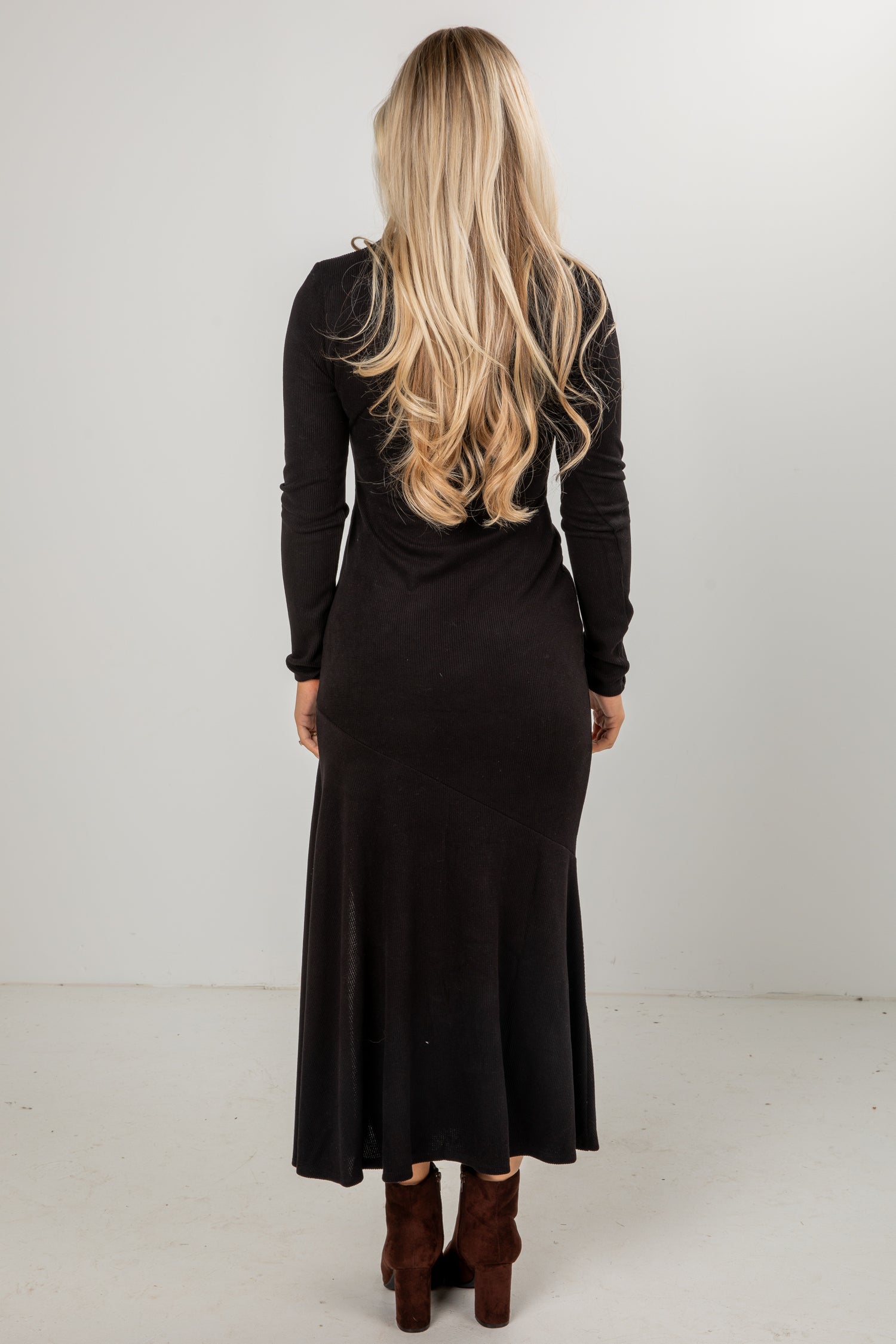 Person wearing a black dress with long sleeves and a fitted silhouette on a white background