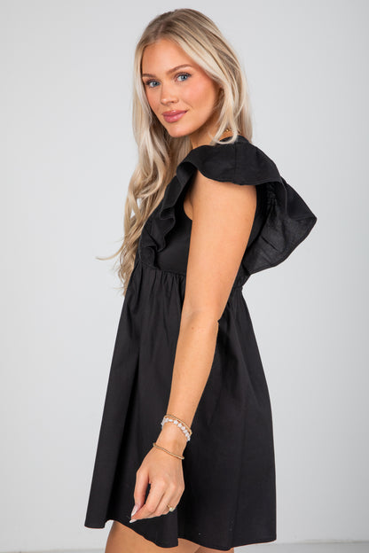 Woman wearing a black dress with ruffled shoulders against a white background