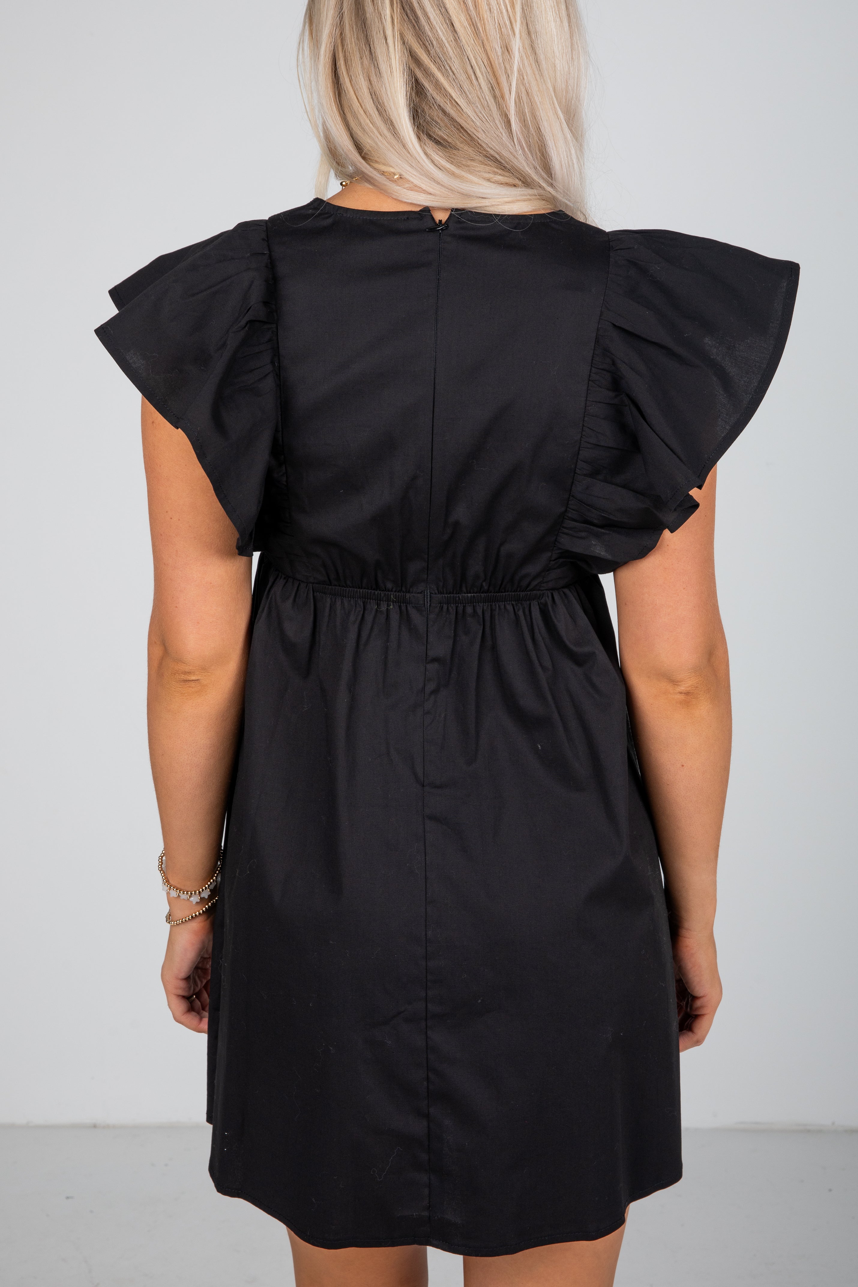 Black dress with ruffled shoulders on a plain background