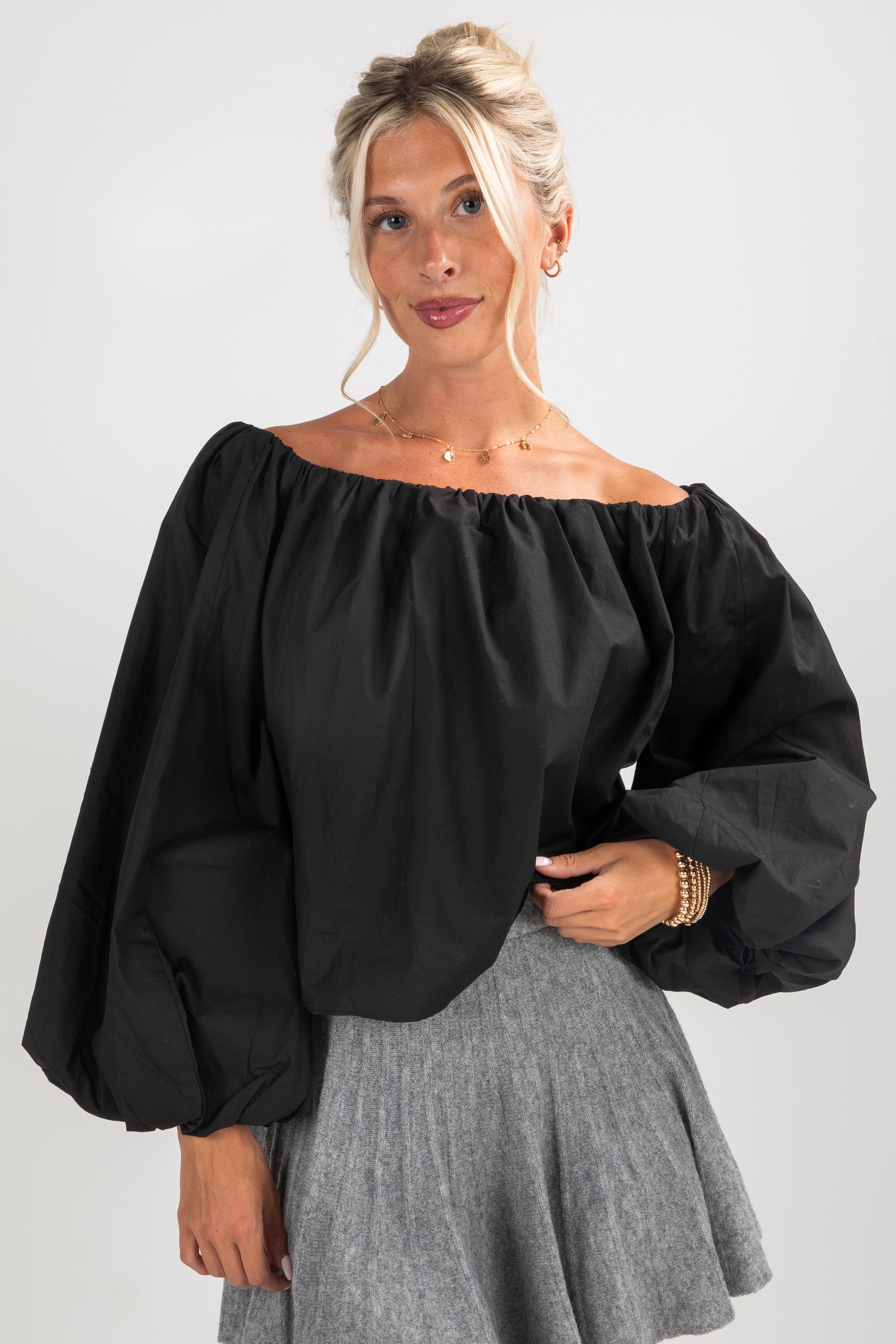 Woman wearing a black off-shoulder top and gray skirt on a white background