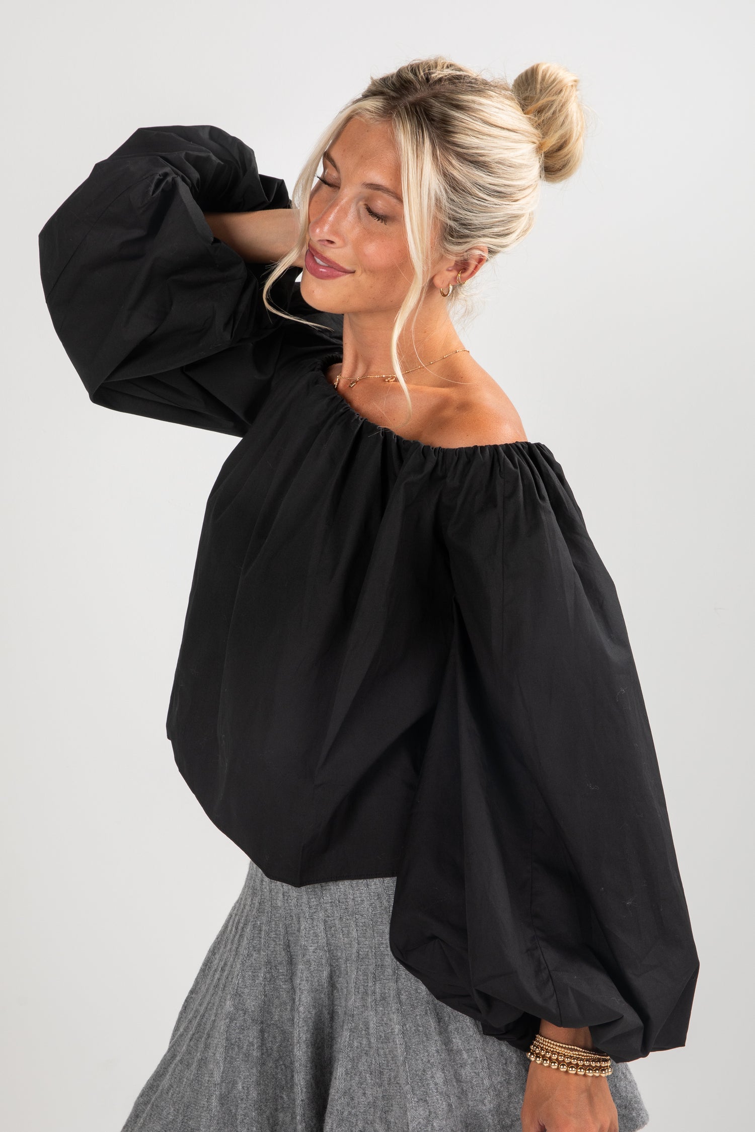 Woman wearing a black off-shoulder top with balloon sleeves on a plain background