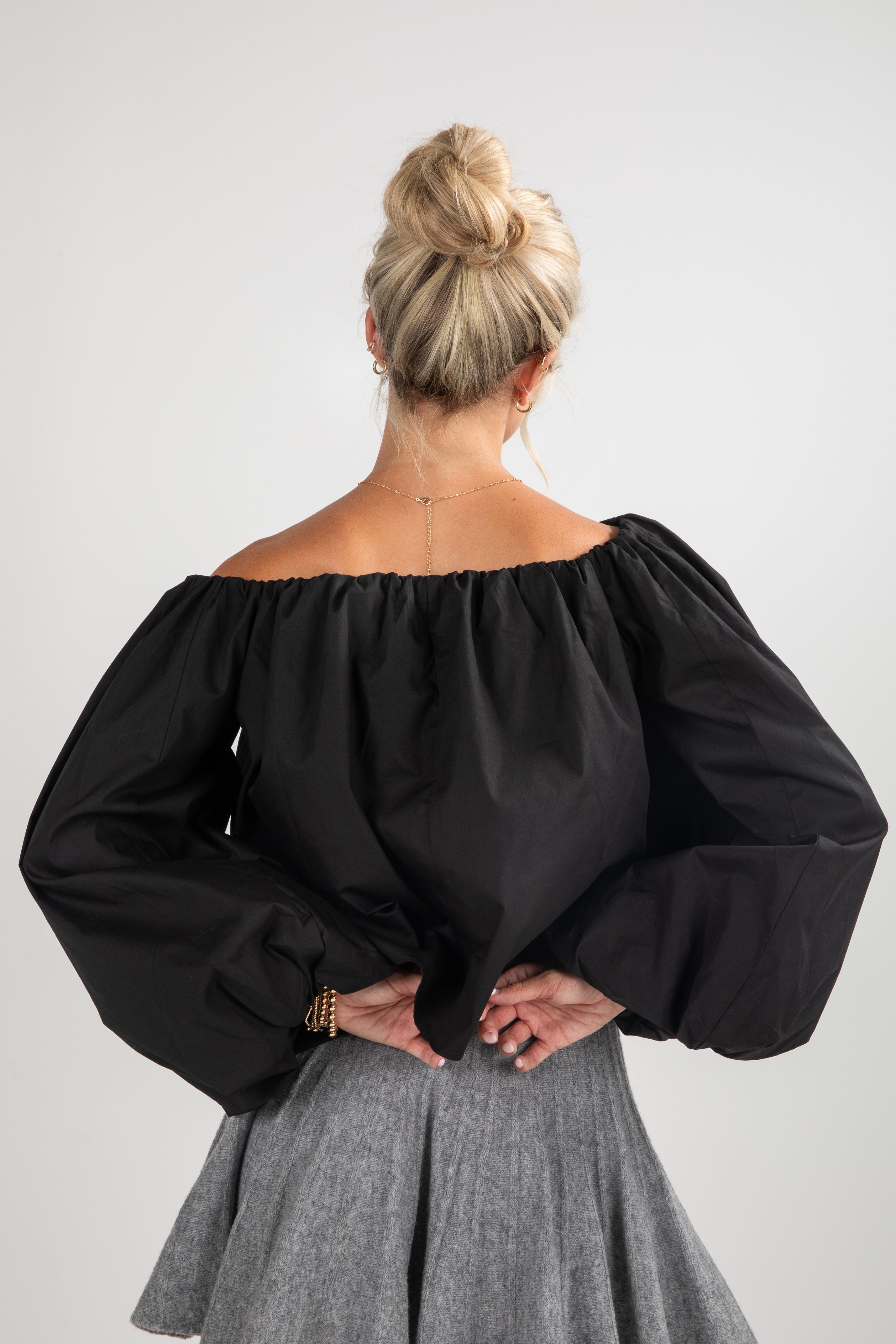 Person wearing a black off-shoulder top and gray skirt on a white background