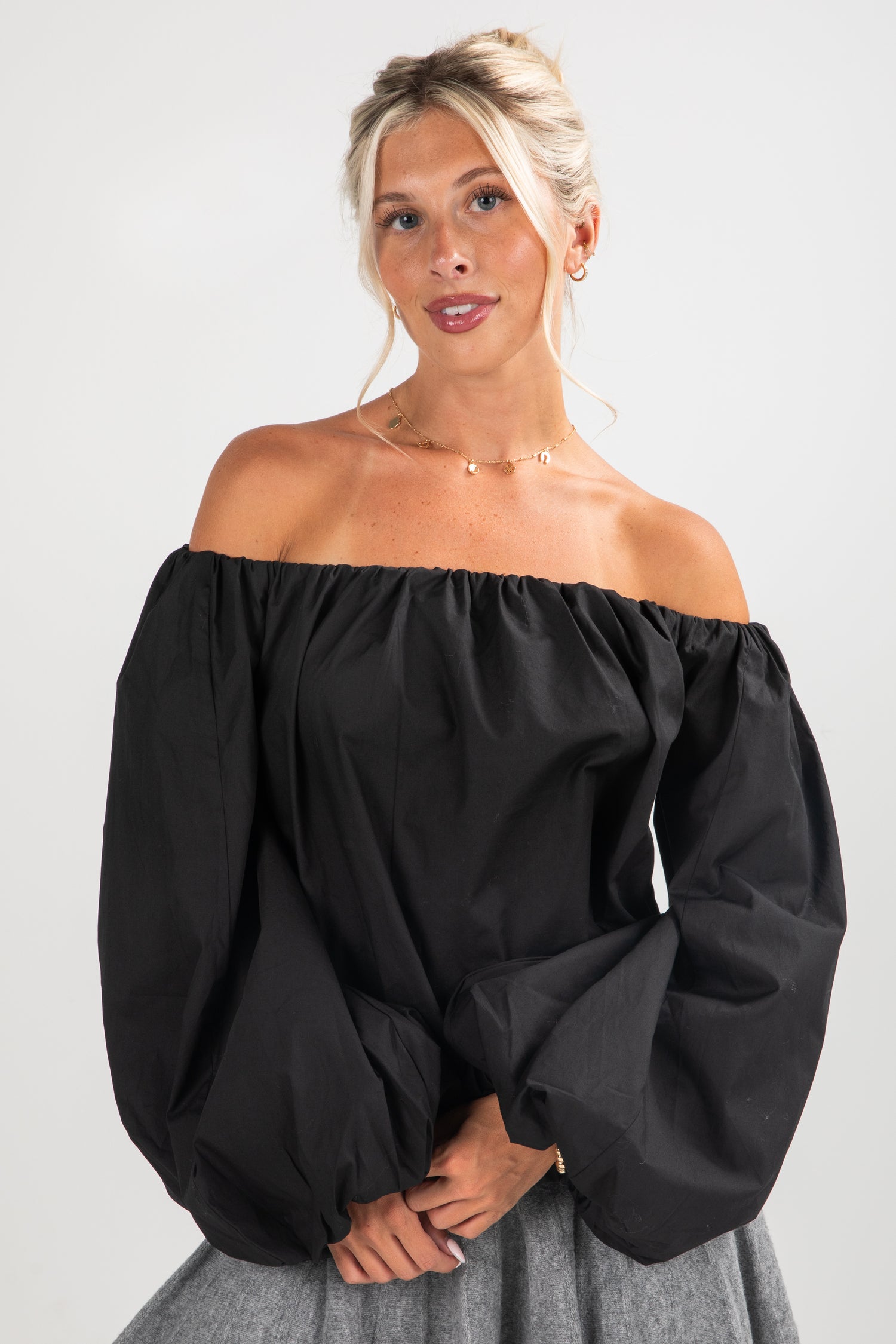 Woman wearing a black off-shoulder top with gray pants on a white background