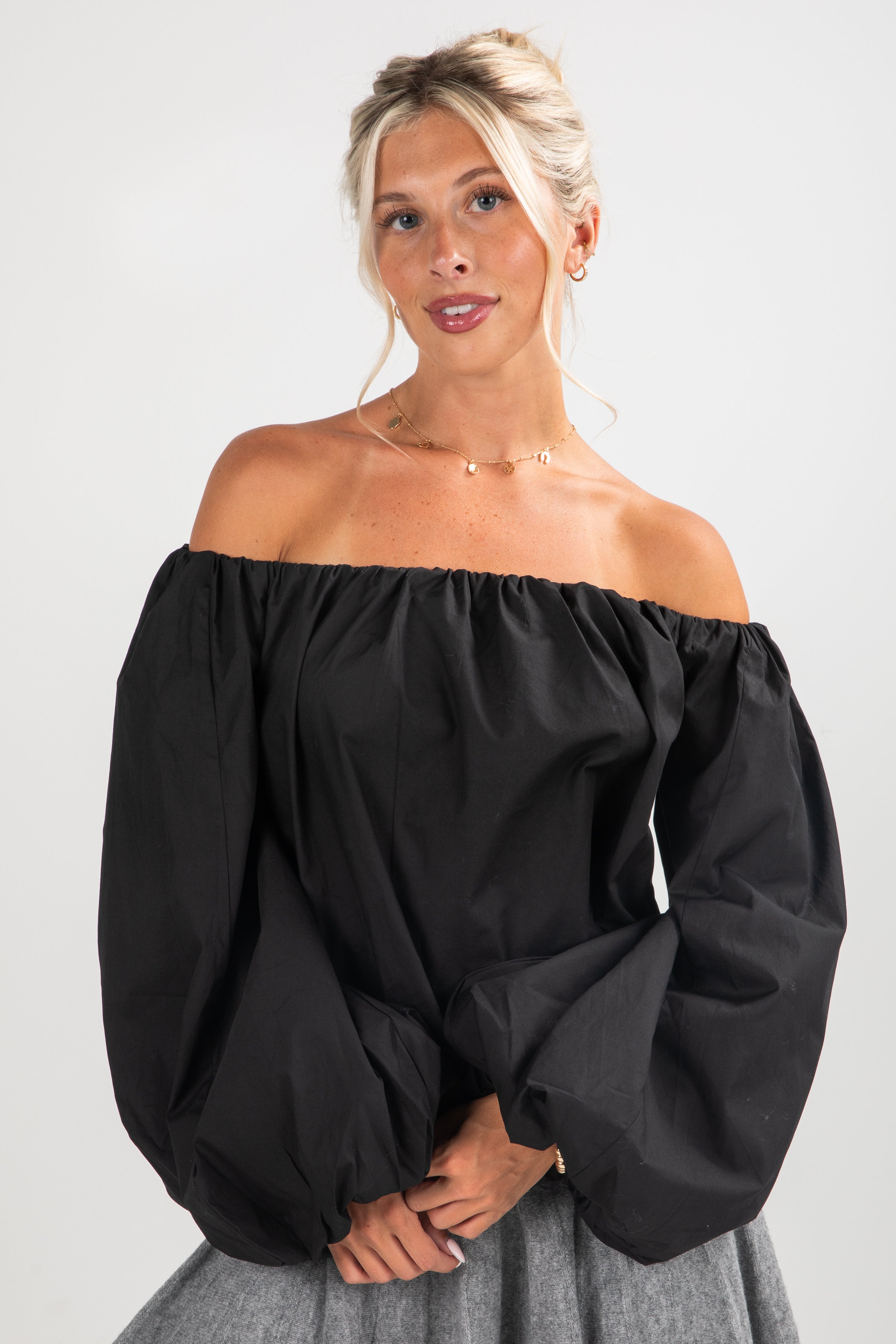 Woman wearing a black off-shoulder top with gray pants on a white background