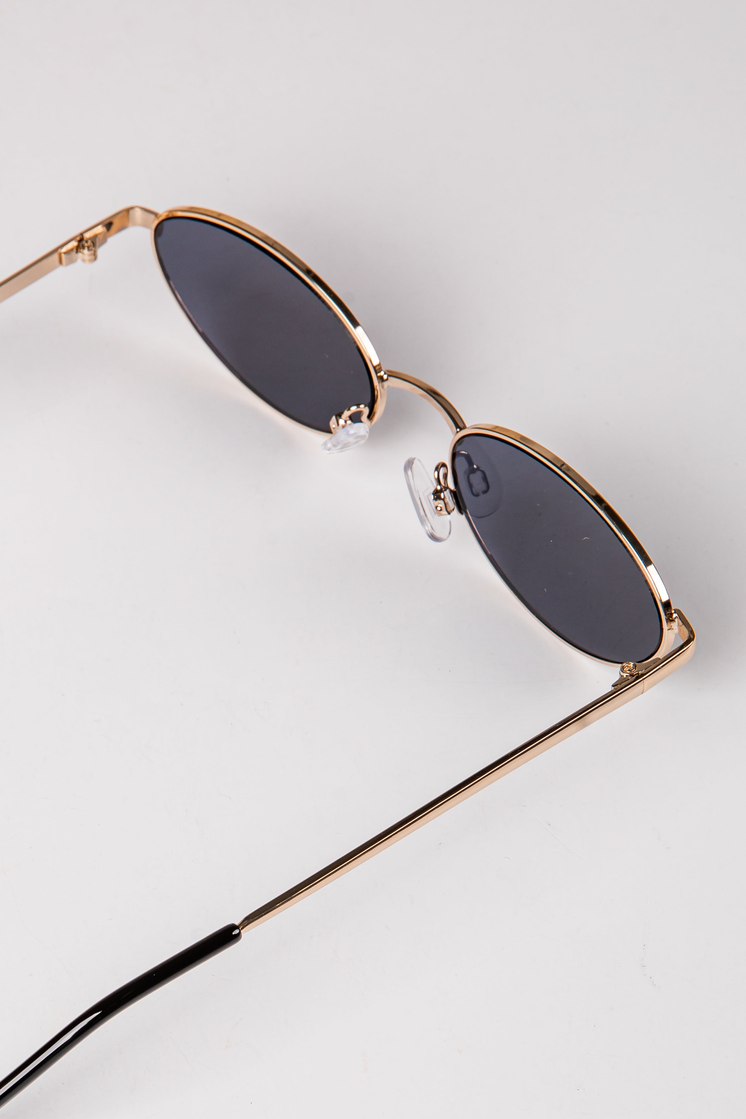 Sunglasses with gold frame and dark lenses on a light gray background