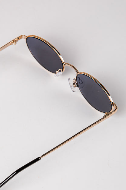Sunglasses with gold frame and dark lenses on a light gray background