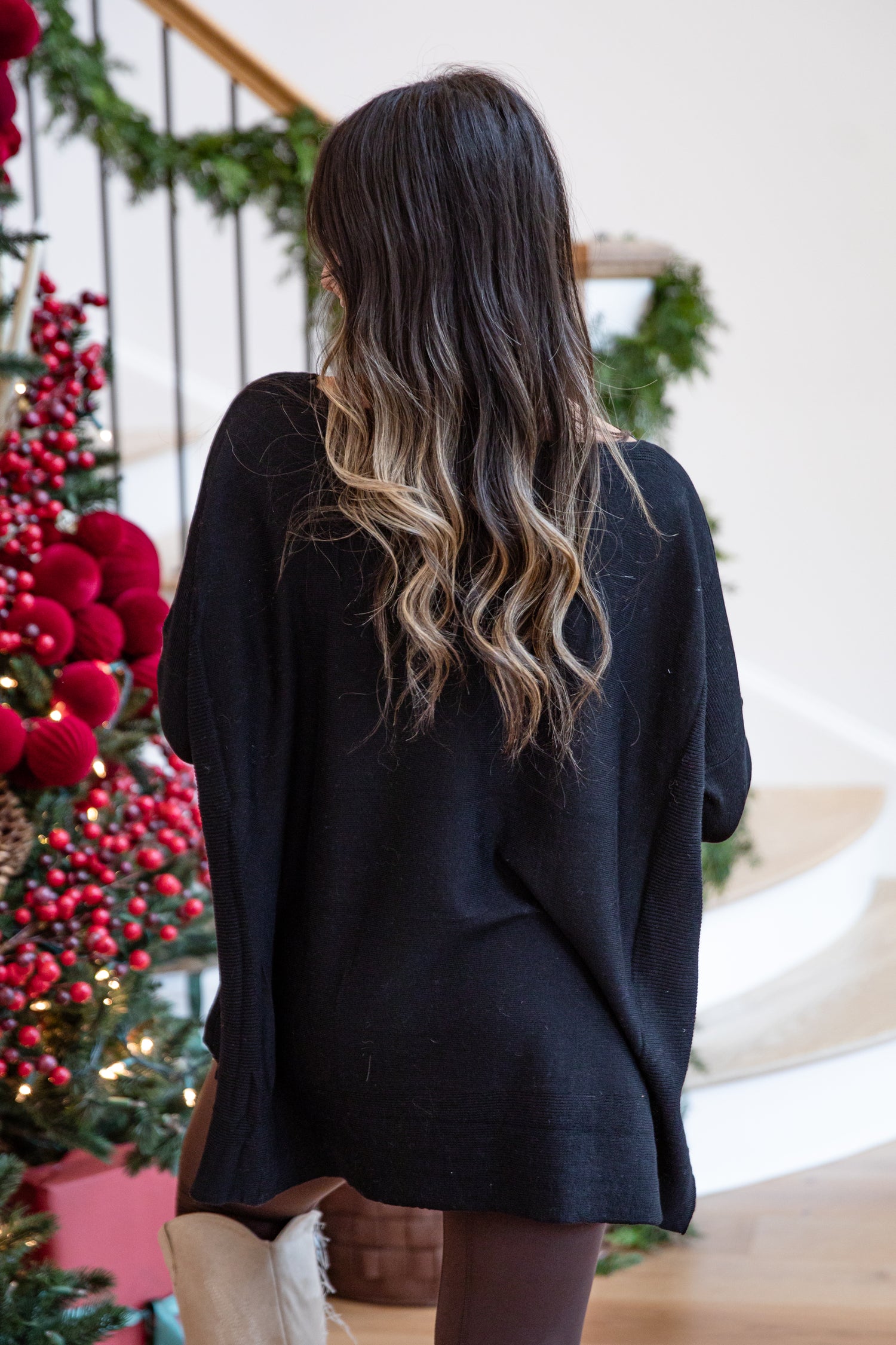 Person wearing a black sweater standing in front of a decorated Christmas tree.