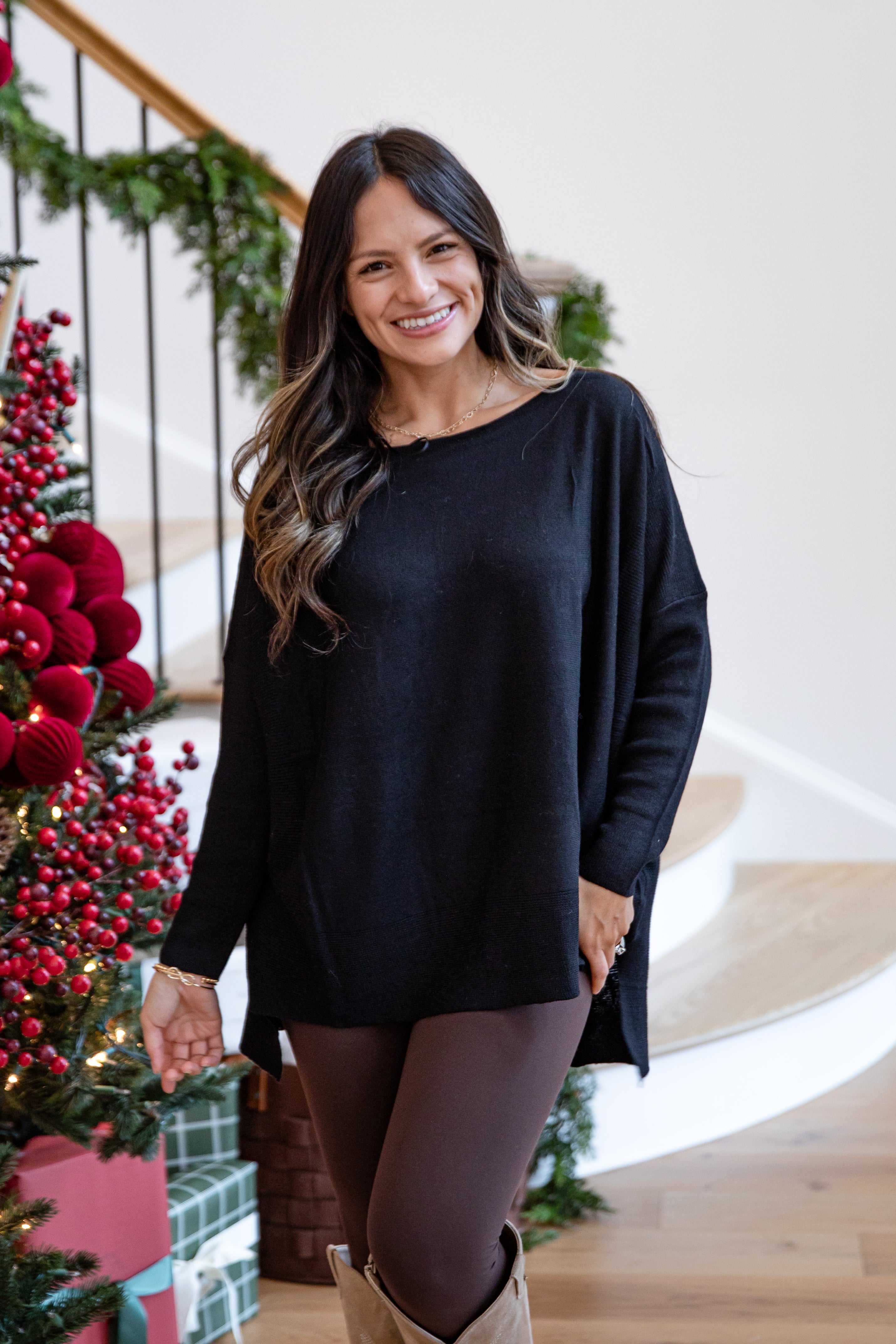 Woman wearing a black sweater standing in front of a decorated Christmas tree.