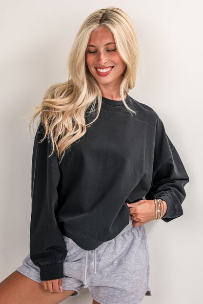 Woman wearing a black sweatshirt and gray shorts against a plain background