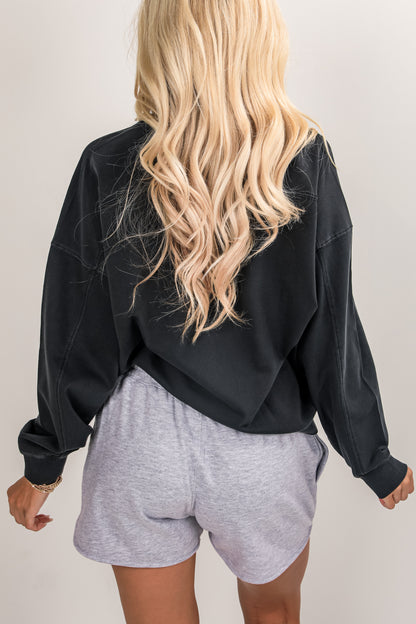 Person wearing a black sweatshirt and gray shorts on a plain background