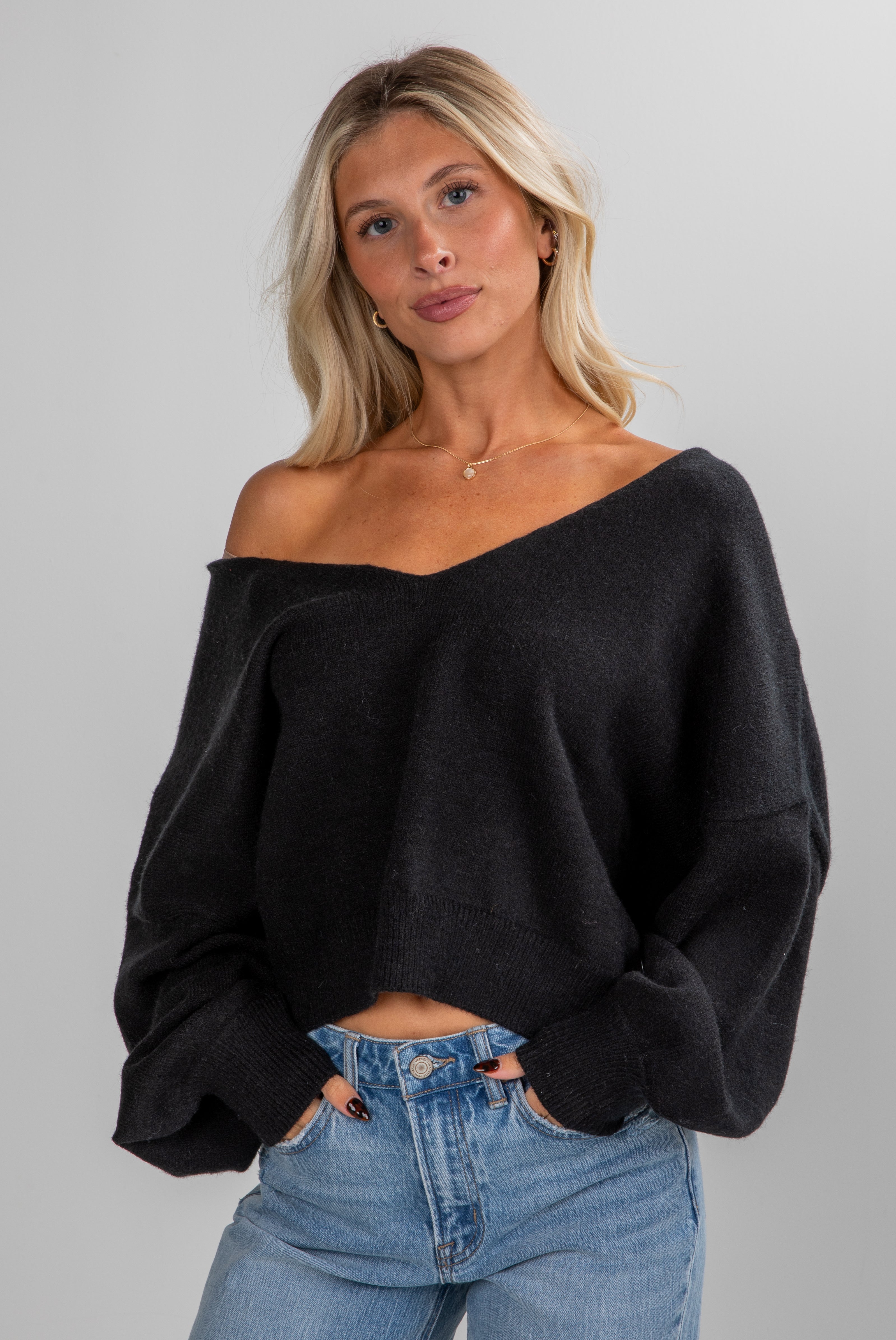 Woman wearing a black off-shoulder sweater and blue jeans on a gray background