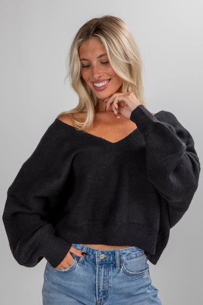 Woman wearing a black sweater and blue jeans against a gray background