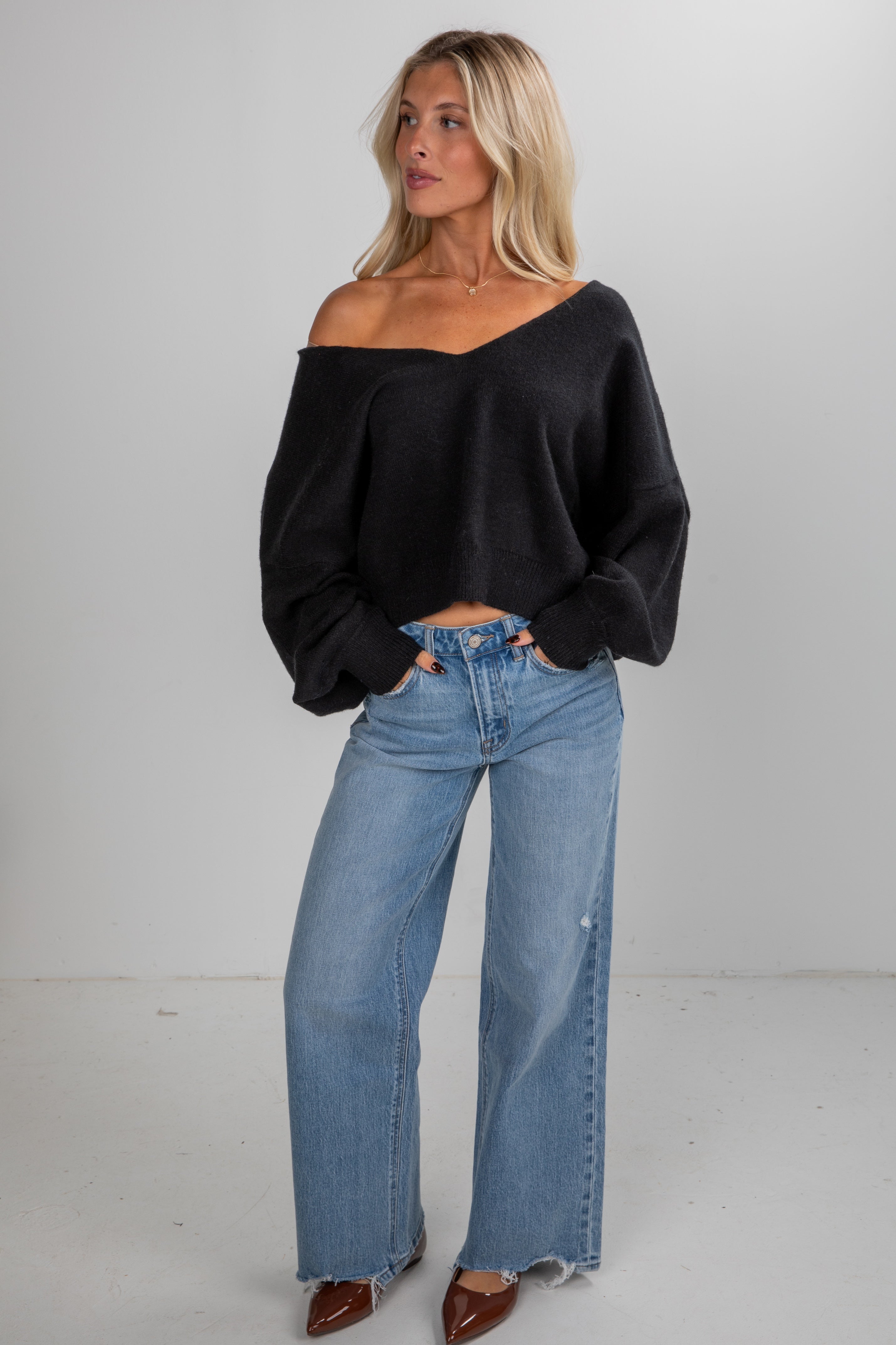 Woman wearing a black off-shoulder top and blue jeans on a white background