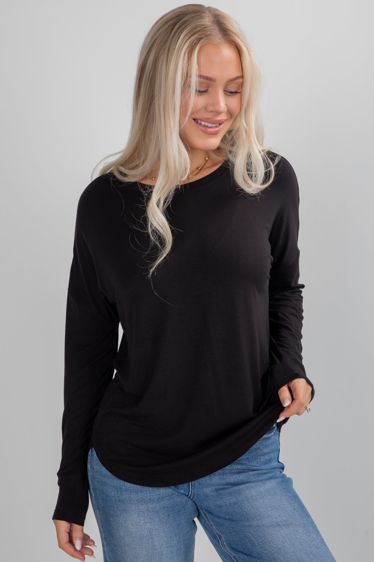 Woman wearing a black long-sleeve top and blue jeans against a gray background