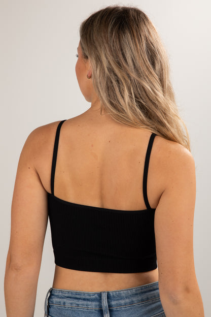 Person wearing a black crop top and blue jeans against a plain background