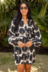 Woman wearing a black and white patterned dress standing in front of green foliage.