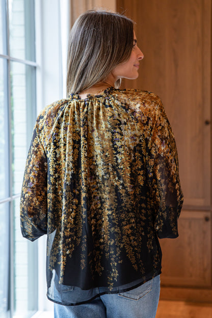 Woman wearing a patterned blouse standing in a room with a window and wooden door.