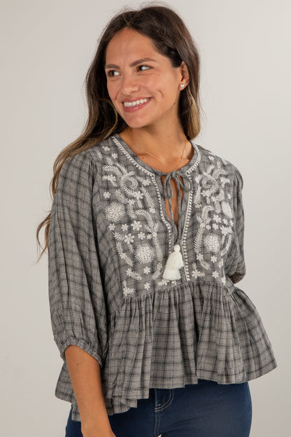 Woman wearing a gray embroidered blouse with a plain background