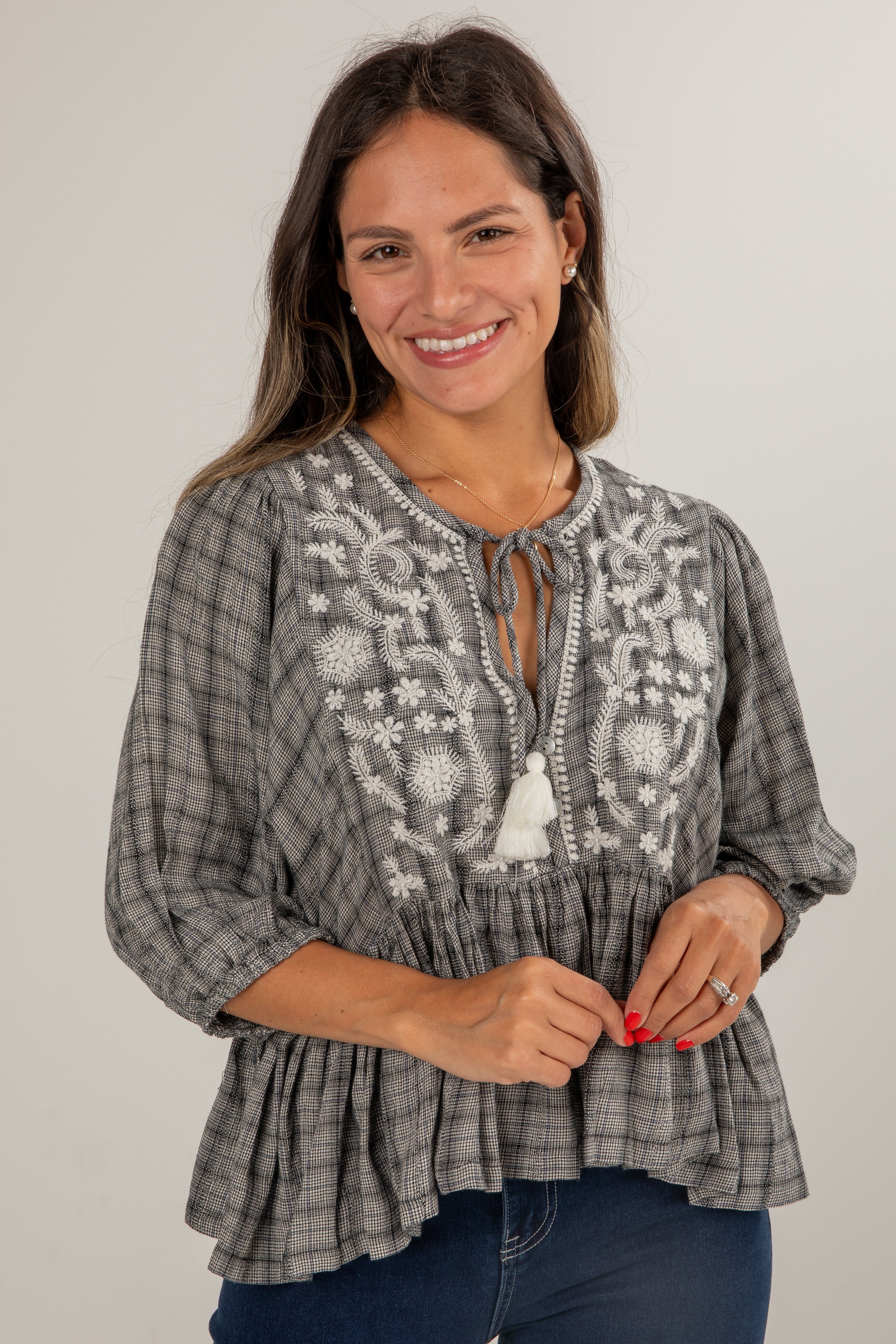 Woman wearing a gray plaid blouse with white embroidery on a plain background