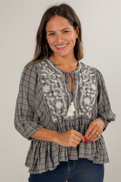 Woman wearing a gray plaid blouse with white embroidery on a plain background