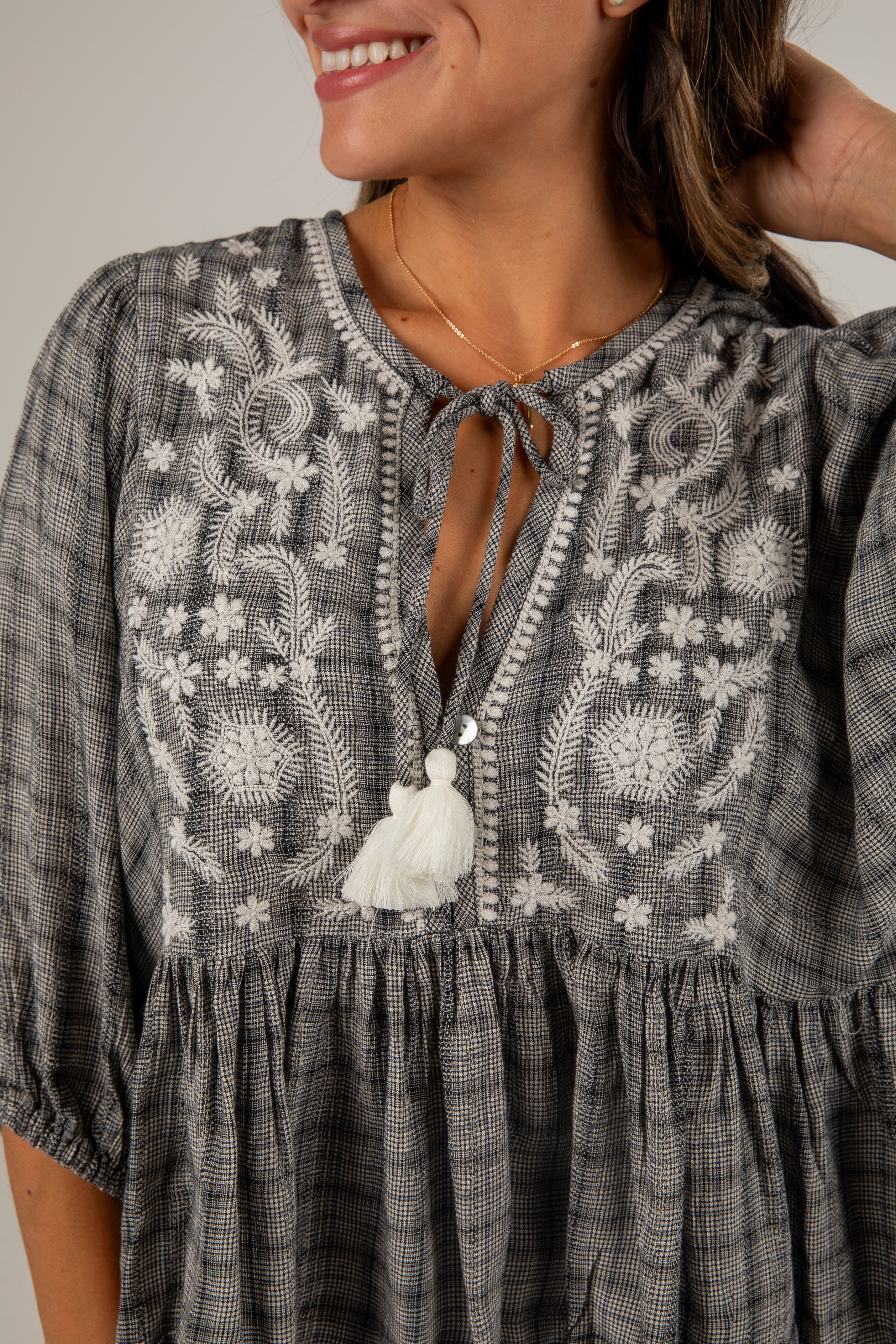 Woman wearing a gray dress with white embroidery and a tassel.