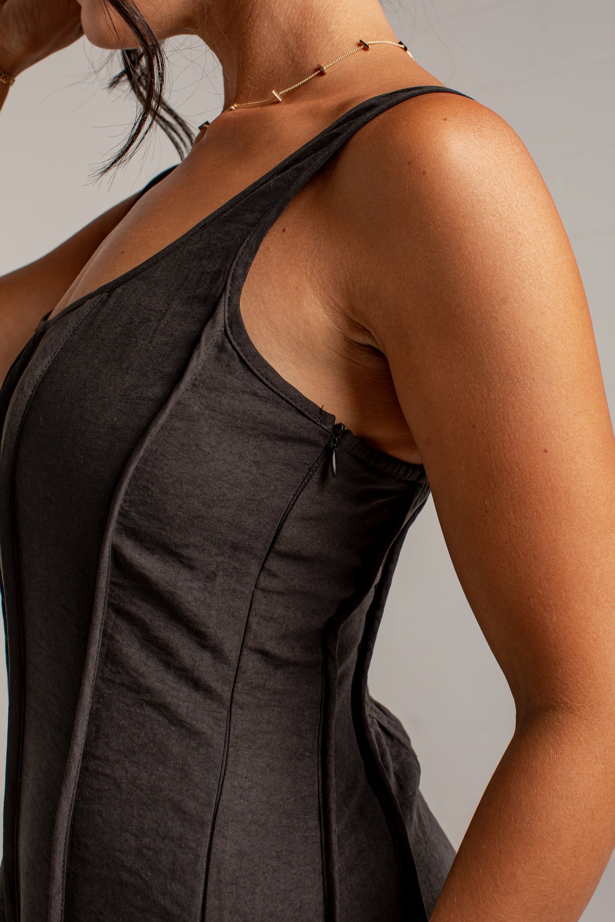 Close-up of a woman wearing a dark charcoal gray sleeveless top, showing the side and back details of the garment against a neutral gray background.