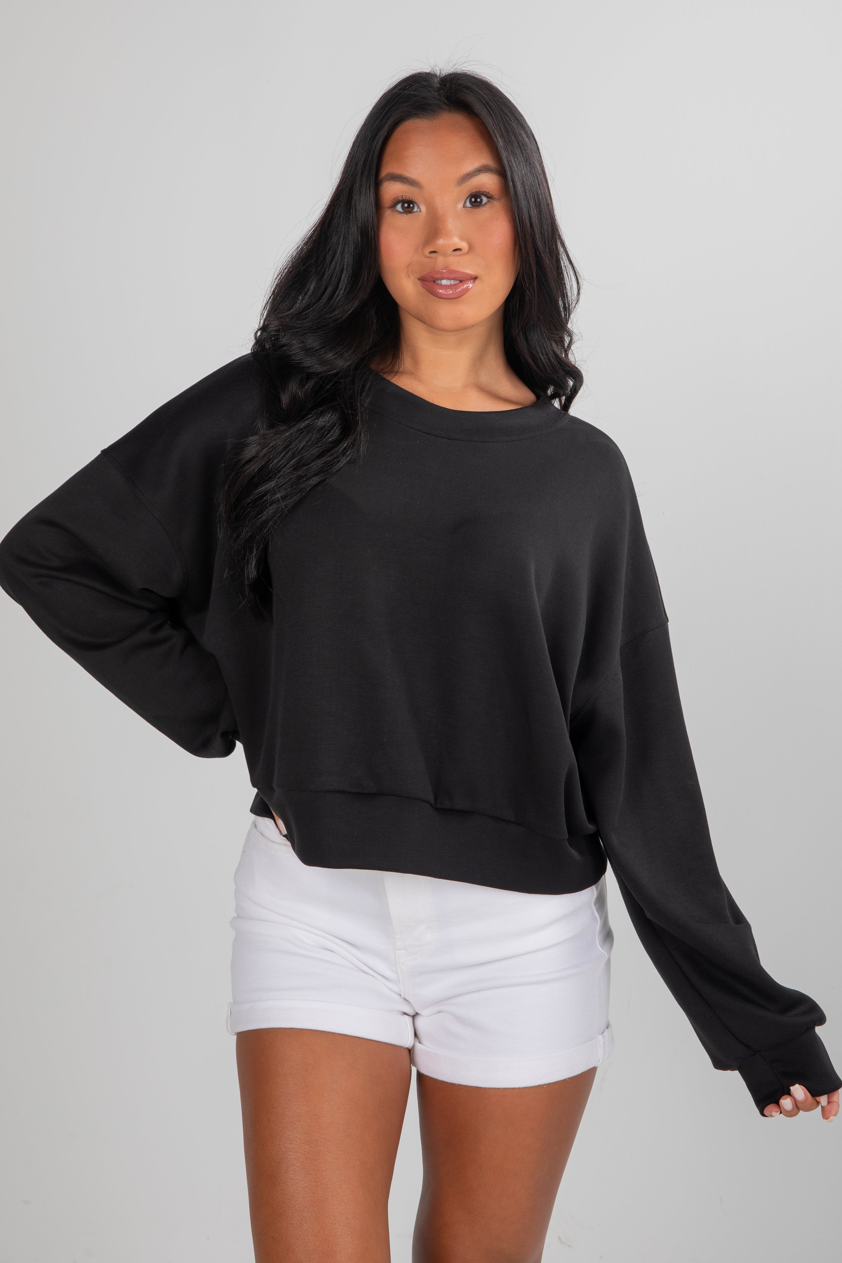 Woman wearing a black oversized sweater and white shorts on a plain background